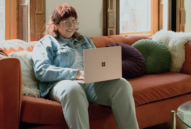 A young woman sitting on a couch, focused on her laptop