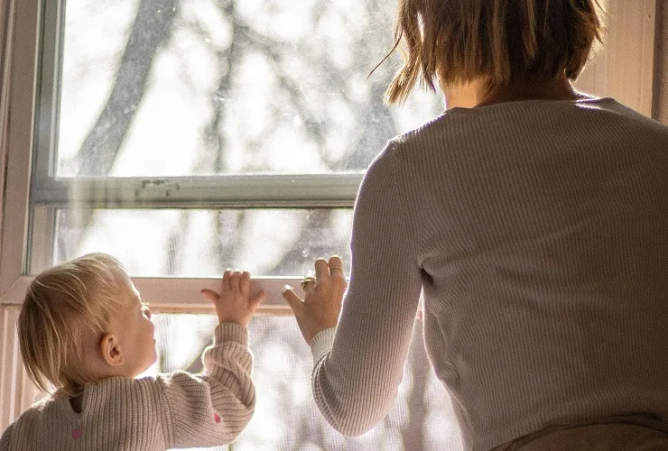 A woman and a child standing together looking out a window