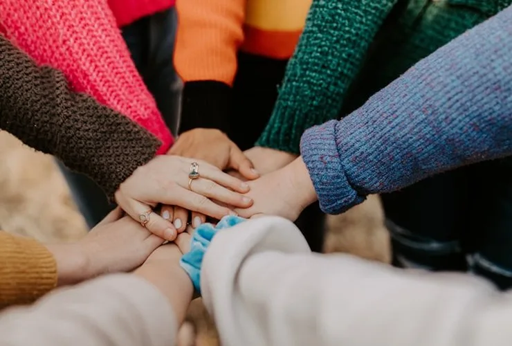 Several individuals of different backgrounds placing their hands on top of each other in a circle