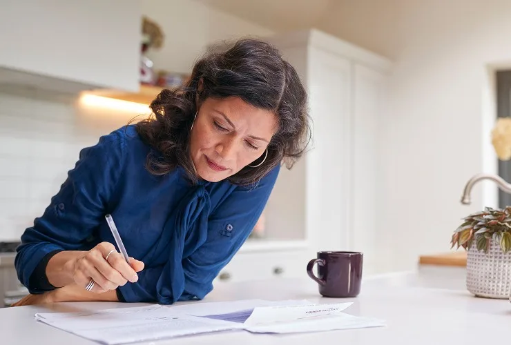 A woman seated at a kitchen table, writing on a piece of paper